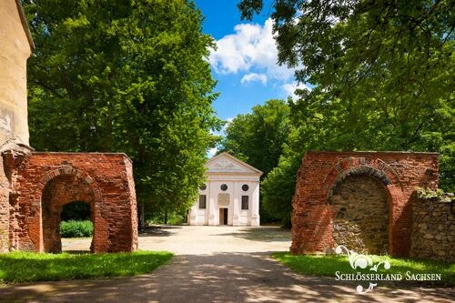 Blick durch zwei Mauerreste auf ein kleines Gebäude des Klosterparks